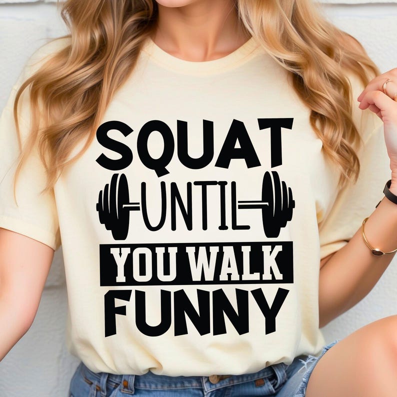 May include: A light yellow t-shirt with black text that reads "Squat Until You Walk Funny" and a black dumbbell graphic.