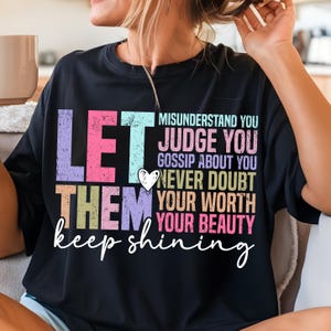 May include: A black t-shirt with a colorful graphic that says "Let them misunderstand you, judge you, gossip about you, never doubt your worth, your beauty, keep shining".