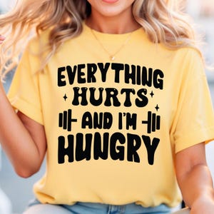 May include: A yellow t-shirt with black text that reads "Everything Hurts + And I'm + Hungry".