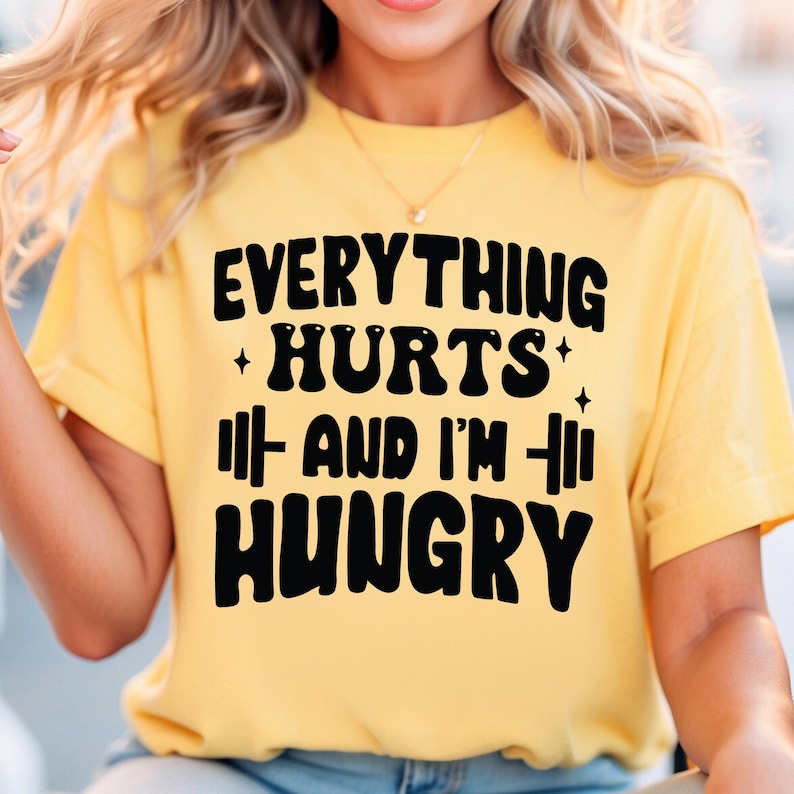 May include: A yellow t-shirt with black text that reads "Everything Hurts + And I'm + Hungry".