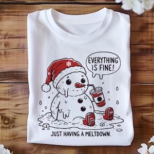 May include: White t-shirt with a cartoon illustration of a melting snowman wearing a red Santa hat and holding a cup. The snowman is surrounded by melting ice and the text "Everything is fine! Just having a meltdown." is printed below the snowman.