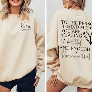 Pu&ograve; includere: Felpa beige con la scritta "You Matter" sul davanti e "To the person behind me: You are amazing, beautiful, and enough. Remember that" sul retro. Girocollo e maniche lunghe.