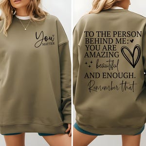 Pu&ograve; includere: Felpa verde oliva con la scritta "You matter" sul davanti. Il retro della felpa riporta il messaggio "To the person behind me: You are amazing, beautiful, and enough. Remember that."