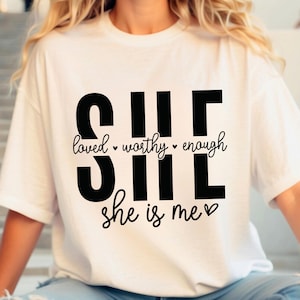 May include: White t-shirt with black text that reads "SHE loved worthy enough she is me" with a heart symbol.
