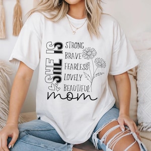May include: White t-shirt with black text that reads "She is strong, brave, fearless, lovely, beautiful mom" with two stylized flower illustrations.