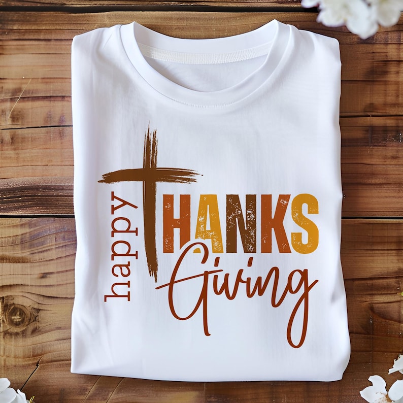 May include: White t-shirt with a brown cross and the text "happy THANKS giving" in orange, brown, and yellow.
