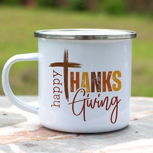 May include: White enamel camping mug with a brown cross and the text "happy THANKS giving" in orange, brown, and yellow.