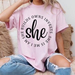 May include: A pink t-shirt with a black circle graphic that says "She is me I am she builds owns invests".