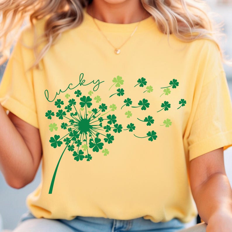 Puede incluir: Una camiseta amarilla con un dise&ntilde;o de diente de le&oacute;n de tr&eacute;bol verde y la palabra "lucky" escrita en cursiva.
