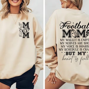 May include: Beige sweatshirt with black text that reads "Football Mom" and "My wallet is empty, my nerves are shot, my voice is hoarse, my schedule is crazy, but my heart is full".