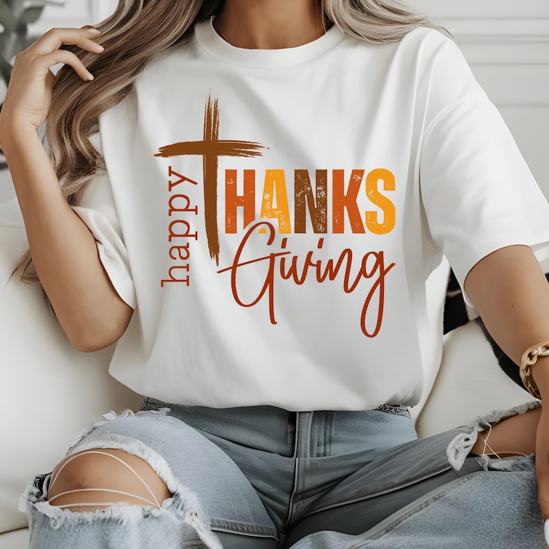 May include: White t-shirt with a brown cross and the text "happy THANKS giving" in orange, yellow, and brown.