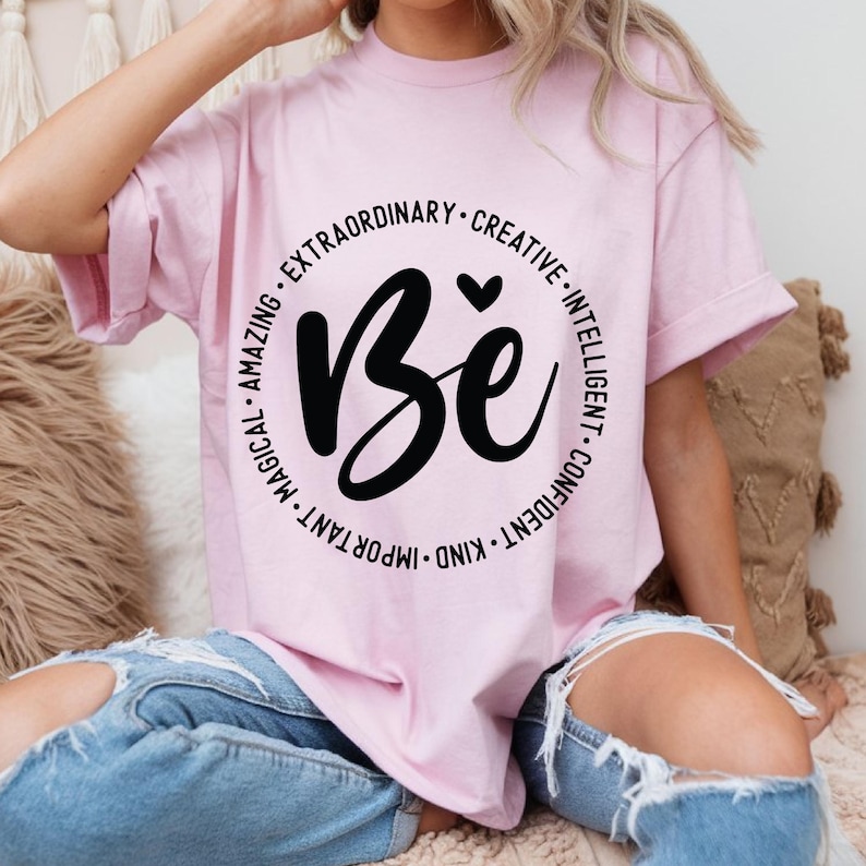 May include: Pink t-shirt with a black circle graphic that says "Be" with the words "important, kind, confident, intelligent, creative, extraordinary, amazing, magical" around the circle.