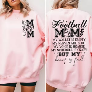May include: Pink sweatshirt with a black graphic that says "Football Mom" and includes a football design. The text below the graphic says "My wallet is empty, my nerves are shot, my voice is hoarse, my schedule is crazy, but my heart is full."