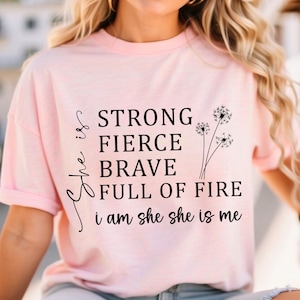 May include: Pink t-shirt with a black graphic that reads "She is strong, fierce, brave, full of fire. I am she, she is me." with three dandelion illustrations.