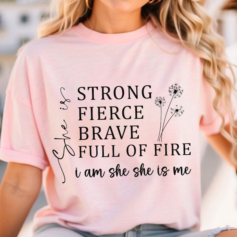 May include: Pink t-shirt with a black graphic that reads "She is strong, fierce, brave, full of fire. I am she, she is me." with three dandelion illustrations.