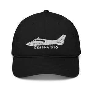 Può includere: Cappellino da baseball nero con un'immagine ricamata bianca di un aereo Cessna 310 e il testo "CESSNA 310".