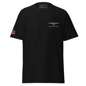 Può includere: T-shirt nera con la scritta "Lockwood AirCam" e una grafica di un aereo sul petto. La manica sinistra presenta la scritta "MAX POWER" in rosso. Una piccola etichetta è visibile sullo scollo.
