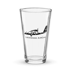 Può includere: Un bicchiere di pinta in vetro trasparente con una silhouette nera di un piccolo aereo e il testo "LOCKWOOD AIRCAM" stampato sul lato.