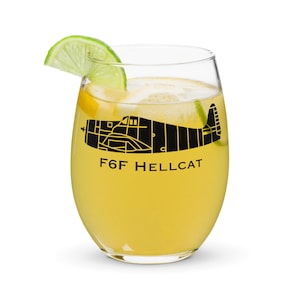 May include: A clear glass with a yellow beverage and a lime wedge. The glass has a black silhouette of a plane with the text "F6F HELLCAT" printed on it.