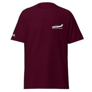 Può includere: Una t-shirt color borgogna con una silhouette bianca di un aereo Beechcraft Baron e il testo "Beechcraft Baron" stampato sul davanti.