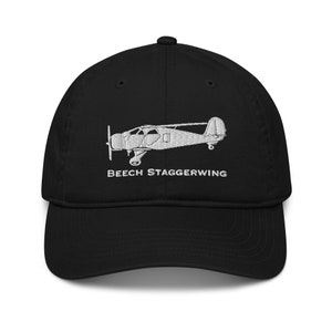 Könnte beinhalten: Schwarze Baseballkappe mit weißer Stickerei eines Beech Staggerwing Flugzeugs. Der Text "Beech Staggerwing" ist unter dem Flugzeug gestickt.