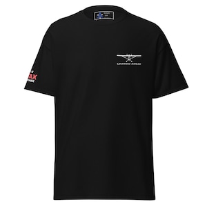 Può includere: T-shirt nero con una grafica di un aereo bianco e il testo "Lockwood Aircam" sul davanti. La manica sinistra ha il testo "Stay in the Max Power" in rosso.