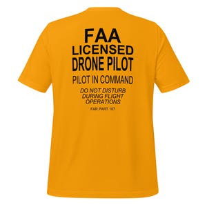 May include: A yellow t-shirt with black text that reads "FAA LICENSED DRONE PILOT PILOT IN COMMAND DO NOT DISTURB DURING FLIGHT OPERATIONS FAR PART 107"