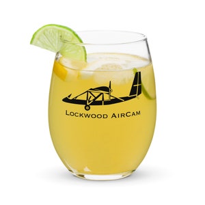 Può includere: Un bicchiere di vino in vetro trasparente con una bevanda gialla e una fetta di lime. Il bicchiere presenta una silhouette nera di un piccolo aereo con la scritta "Lockwood Aircam" stampata su di esso.