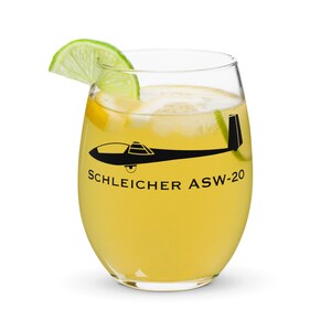 May include: A clear glass with a yellow beverage and a lime wedge. The glass has a black silhouette of a glider with the text "SCHLEICHER ASW-20" printed on it.
