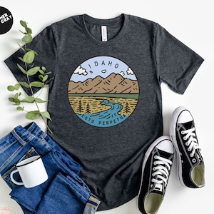 May include: A dark heather grey t-shirt with a graphic design of a mountain range and river with the text "Idaho Esto Perpetua" in a circle.