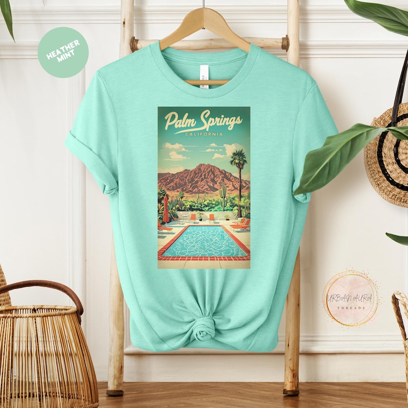 Peut inclure: Un t-shirt turquoise avec un motif vintage d'une piscine et de palmiers. Le motif indique "Palm Springs, Californie".
