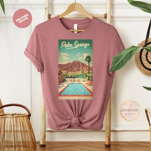 Peut inclure: Un t-shirt en mauve chin&eacute; avec un graphique vintage d'une piscine et de palmiers. Le graphique indique "Palm Springs, Californie".
