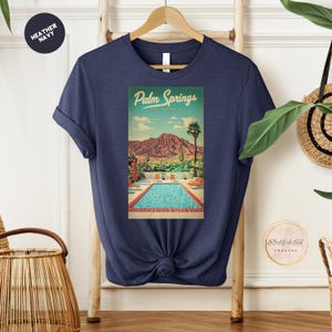 Peut inclure: Un t-shirt bleu marine avec un graphique vintage d'une piscine et de palmiers &agrave; Palm Springs, Californie. Le texte "Palm Springs, Californie" est imprim&eacute; sur le graphique.