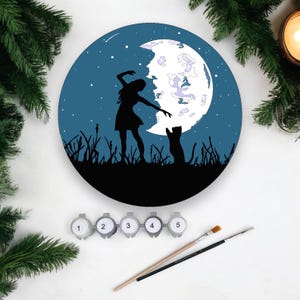 May include: A paint by numbers kit depicting a silhouette of a person dancing with a cat under a crescent moon. The background is a dark blue night sky with stars.