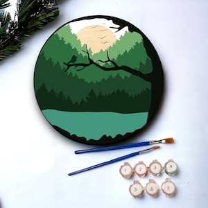 May include: A round wooden painting of a forest scene with a lake, a sun, and birds. The painting is divided into seven numbered sections for paint by numbers.