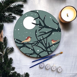 May include: A round wooden painting with a winter scene. The painting features a blue-green background with a white moon, a black tree with branches, and two red birds. The painting is surrounded by four small paint pots labeled 1, 2, 3, and 4.