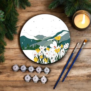 Puede incluir: Un kit de pintura por números que representa un paisaje de invierno con una cordillera nevada y un campo de crocus blancos y amarillos. El kit incluye ocho botes de pintura, dos pinceles y un lienzo redondo.