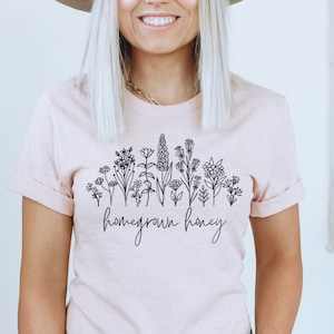 May include: A pink t-shirt with a floral design and the text "homegrown honey" in black.