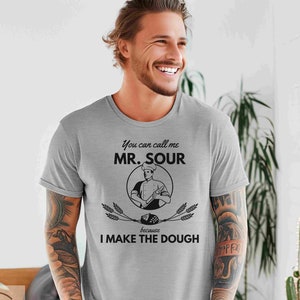 May include: A gray t-shirt with a black graphic that says "You can call me Mr. Sour because I make the dough". The graphic features a cartoon chef holding a rolling pin and a loaf of bread.