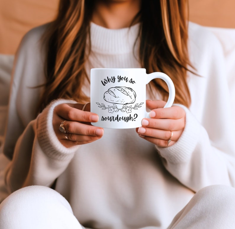 Peut inclure: Une tasse en c&eacute;ramique blanche avec une illustration en noir et blanc d'une miche de pain et le texte "Why you so sourdough?"