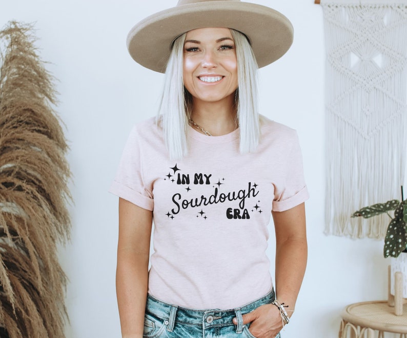 K&ouml;nnte beinhalten: Ein rosa T-Shirt mit dem Text "In My Sourdough Era" in schwarzer Schrift mit kleinen Sternen um den Text.