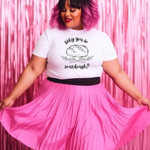 Peut inclure: Un t-shirt blanc avec un motif noir repr&eacute;sentant un pain et le texte "Why you so sourdough?" Le mannequin porte une jupe pliss&eacute;e rose et a les cheveux roses.