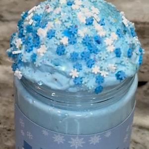 May include: A blue glass jar filled with light blue slime topped with white and blue snowflake sprinkles. The jar has a label that reads "Blueberry Blizzard" with a snowman graphic.