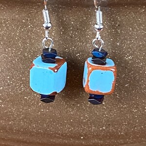 Può includere: Un paio di orecchini pendenti in argento con perline cubiche in ceramica blu e marrone. Le perline hanno una superficie screziata e testurizzata.