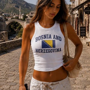 Könnte beinhalten: Ein weißes ärmelloses Tanktop mit dem Schriftzug "BOSNIA AND HERZEGOVINA" in dunkelblauen Buchstaben, zentriert über und unter einer Grafik der Nationalflagge von Bosnien und Herzegowina, die ein gelbes Dreieck und ein blaues Feld zeigt.