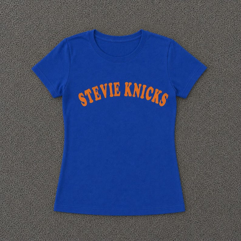 Pu&ograve; includere: Una t-shirt a maniche corte di colore blu reale con la scritta STEVIE KNICKS stampata in un carattere arancione arcuato e audace sul petto. Il capo presenta un classico girocollo e un orlo dritto, offrendo un design semplice e pulito.