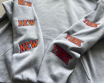 May include: Gray hooded sweatshirt with the words "NEW YORK" embroidered on the sleeves in orange and blue lettering.
