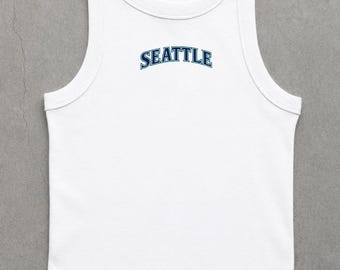 May include: White tank top with a rounded neckline and a sleeveless design. The word "SEATTLE" is arched across the chest in blue lettering.