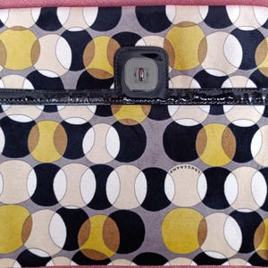 May include: A rectangular clutch with a repeating pattern of overlapping circles in black, white, tan, and yellow. The clutch has a black patent leather trim and a black clasp. The brand name "LONGCHAMP" is visible on the bottom.
