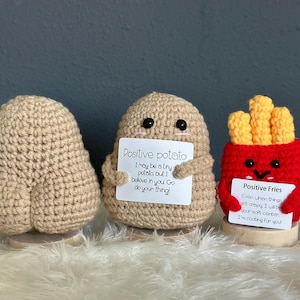 May include: Three crocheted plush toys, a potato, a potato, and a box of french fries, each holding a sign with a positive message. The potato says "Positive potato I may be a tiny potato but I believe in you Go do your thing!" The fries say "Positive Fries Even when things get crazy I will be your soft center. I'm rooting for you."